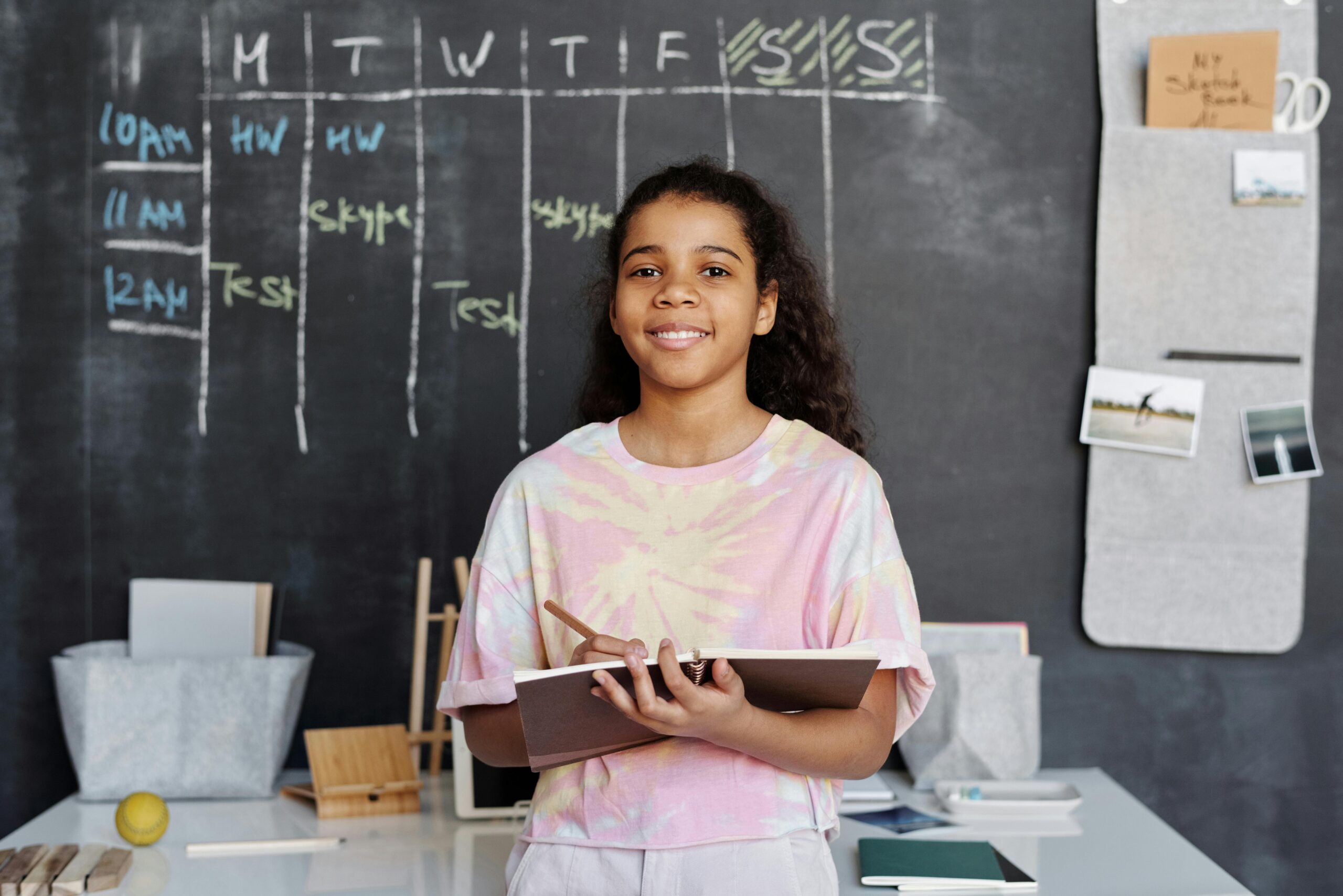 student writing in a notebook looks up to smile for the camera